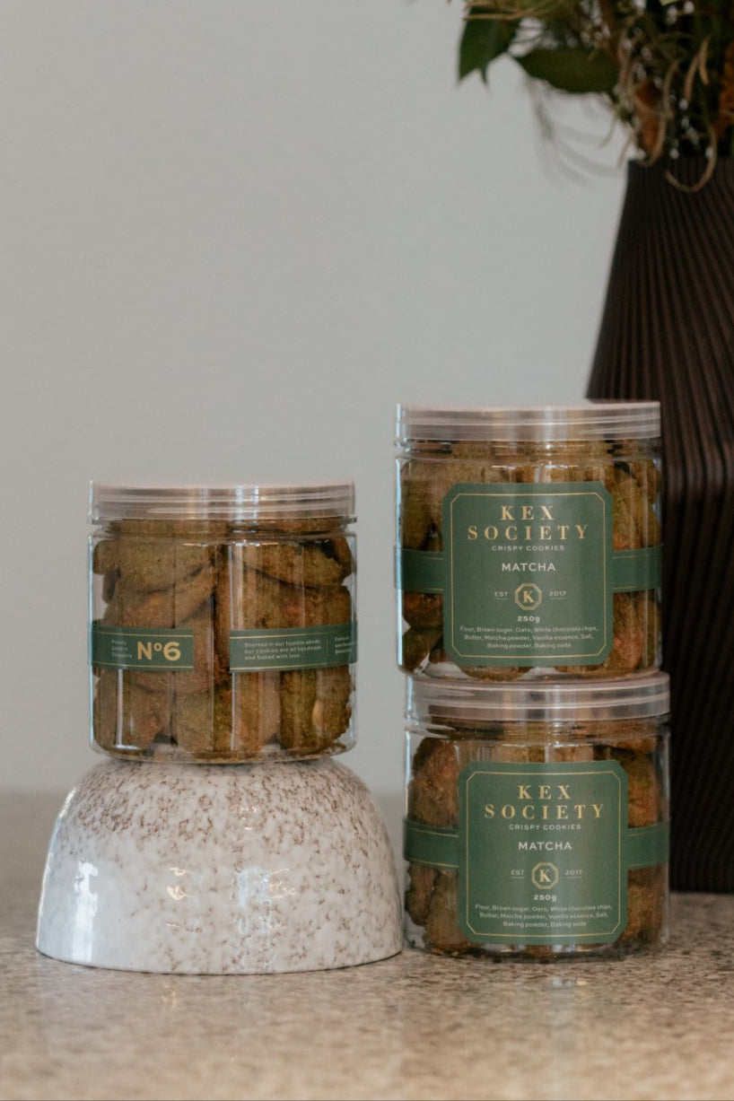 Clear  Kex Society 250g jars containing matcha white chocolate cookies on a table, with branded labels on the jars.