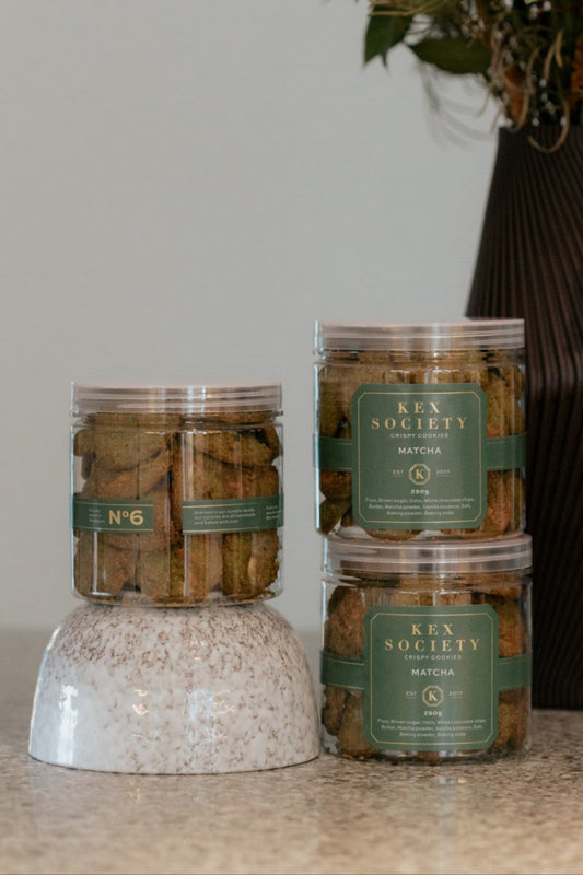 Clear  Kex Society 250g jars containing matcha white chocolate cookies on a table, with branded labels on the jars.