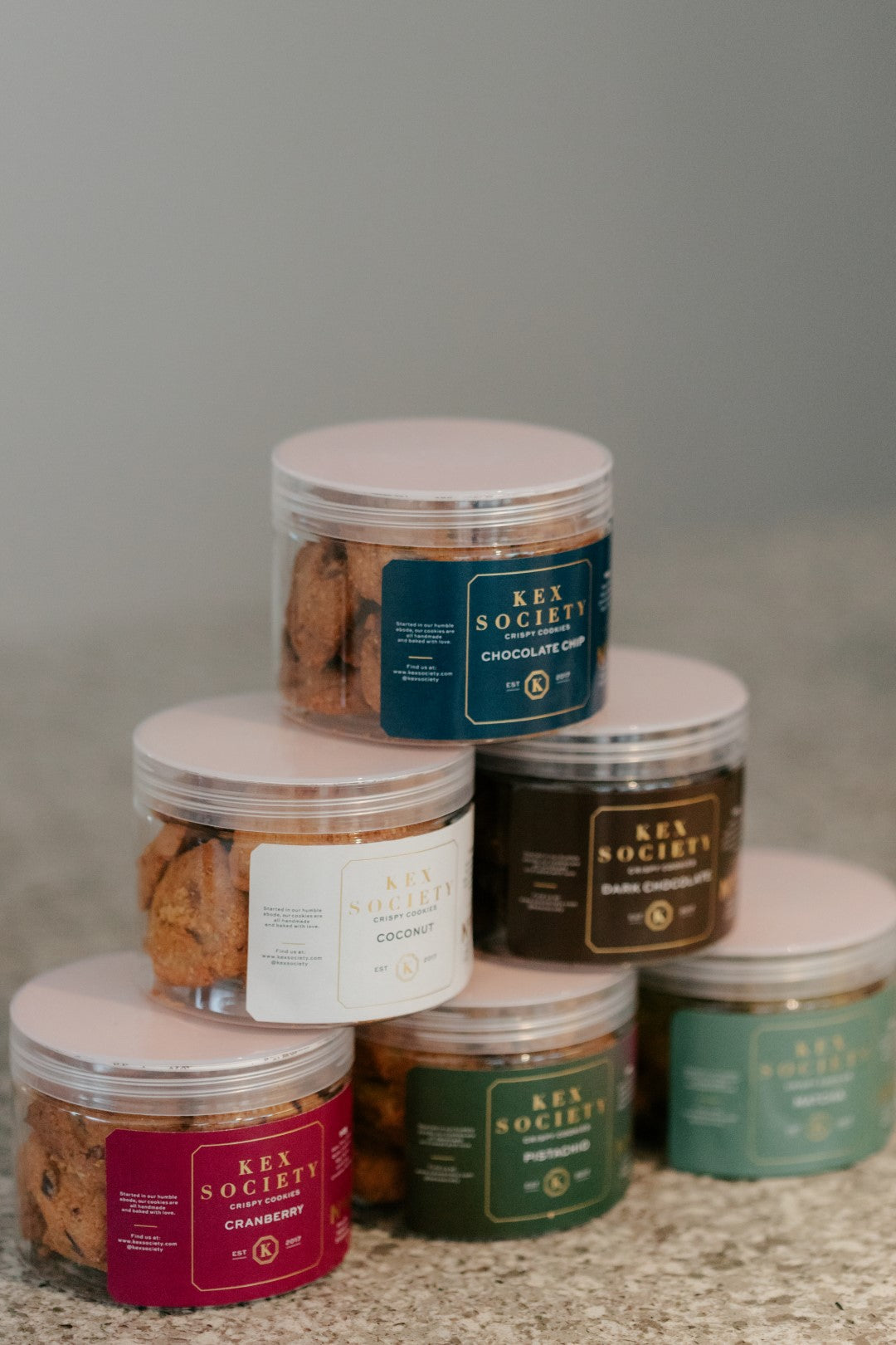 Stack of 110g jars with various flavors from Key Society on a neutral background
