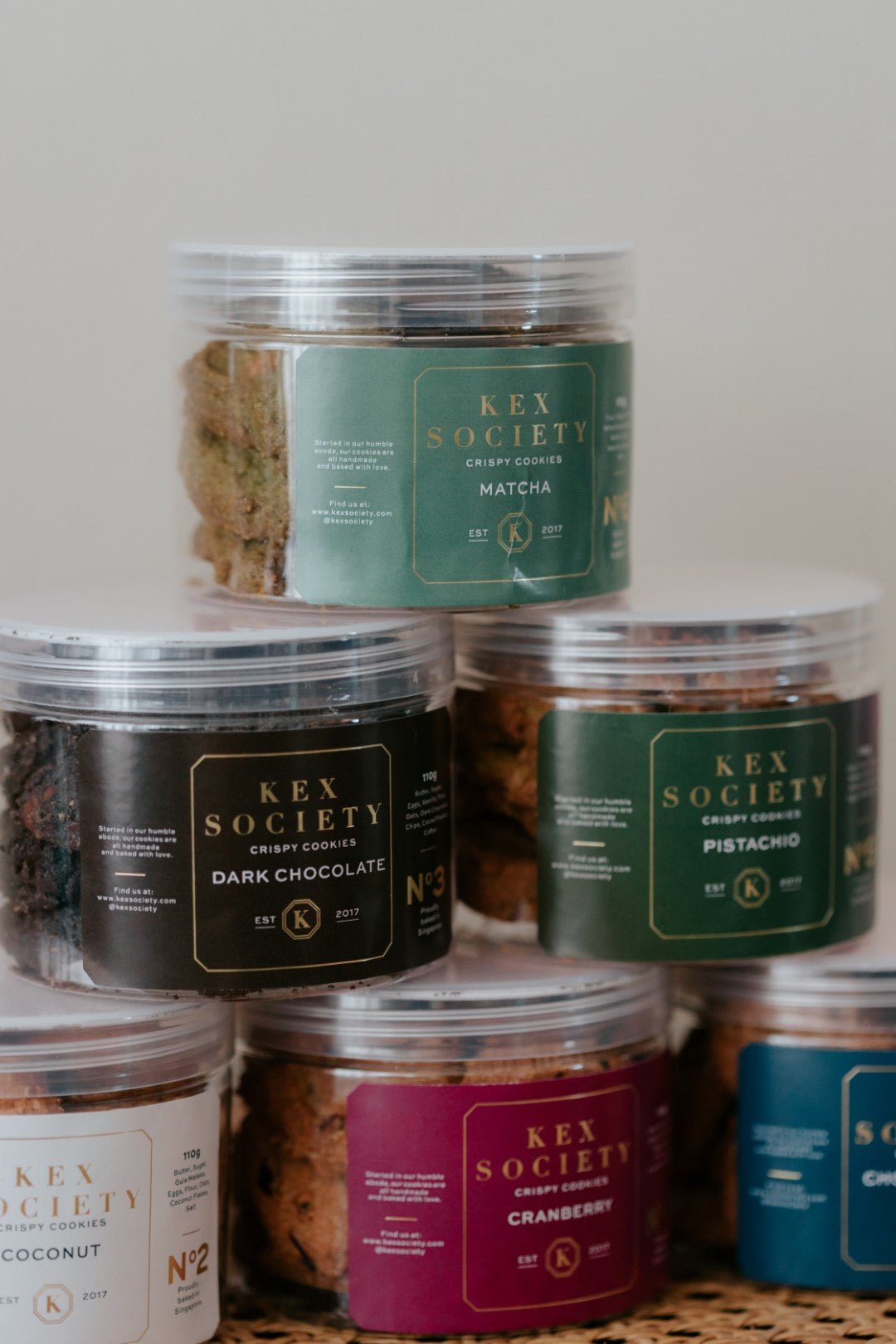 Stack of Kex Society 110g cookie jars with various flavors on a neutral background