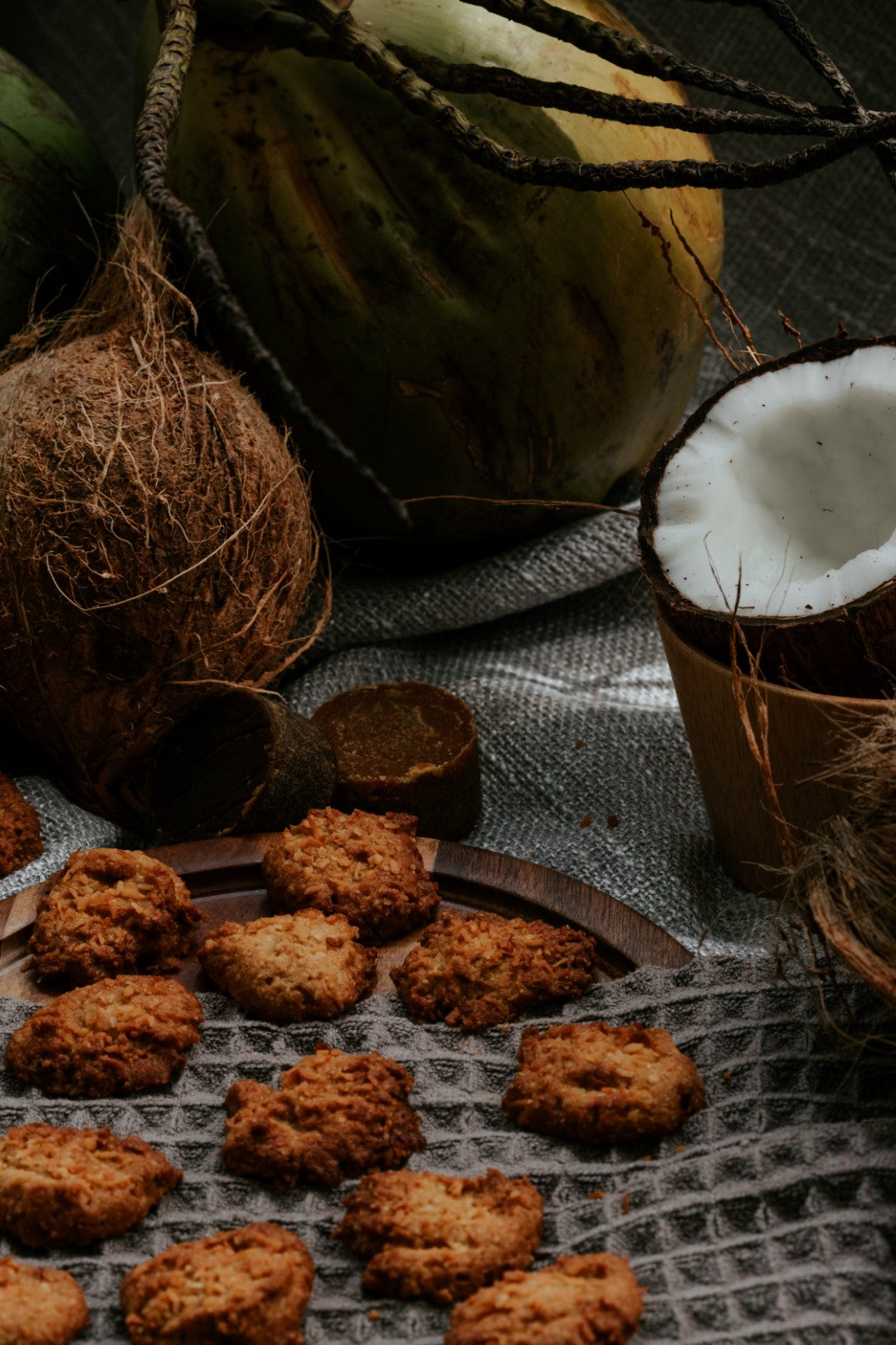 Scattered Kex Society crispy gula melaka coconut cookies displayed among fresh coconuts and gula melaka blocks.