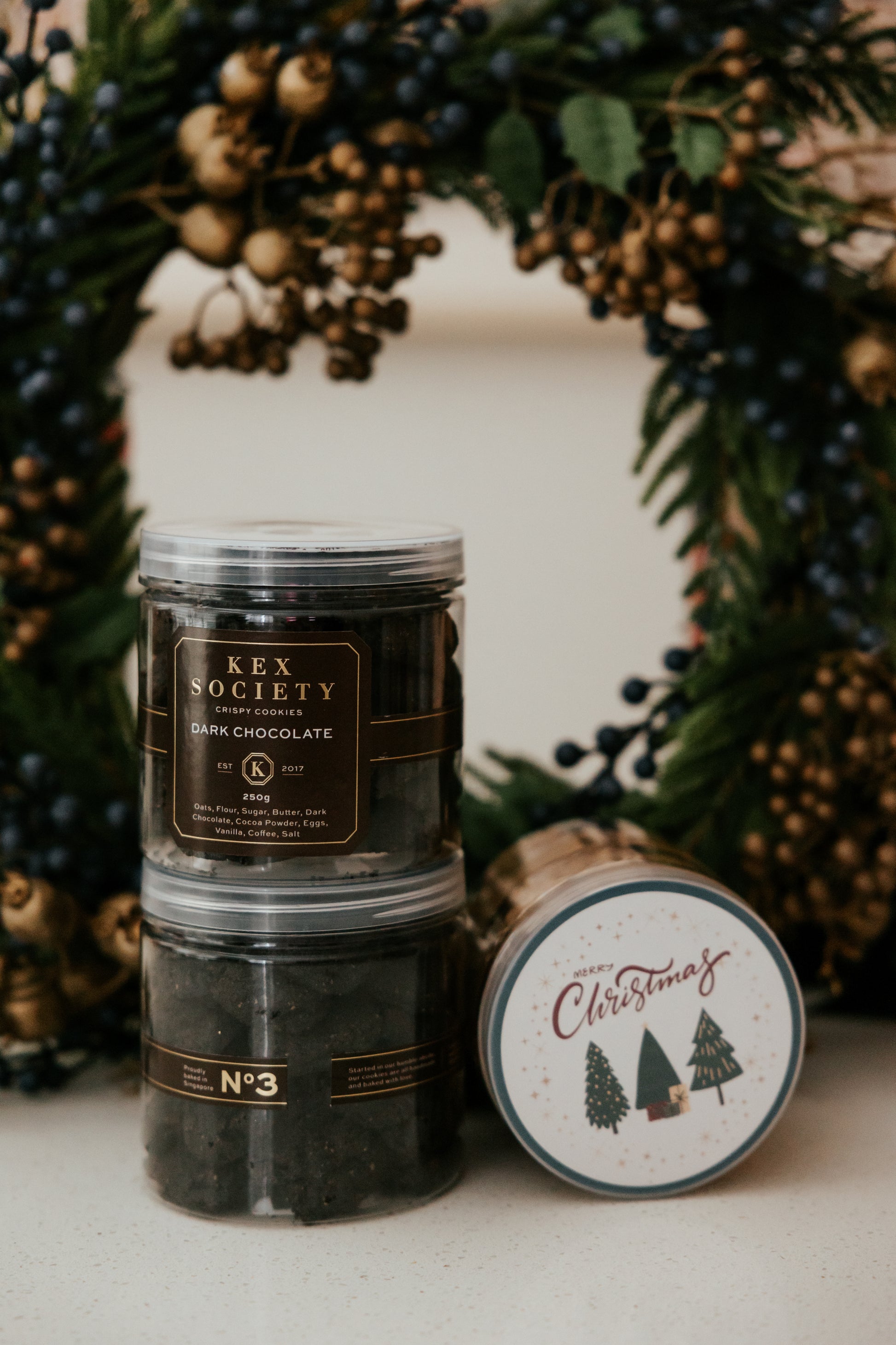 Stack of Kex Society Dark chocolate cookies with a decorative Christmas wreath in the background