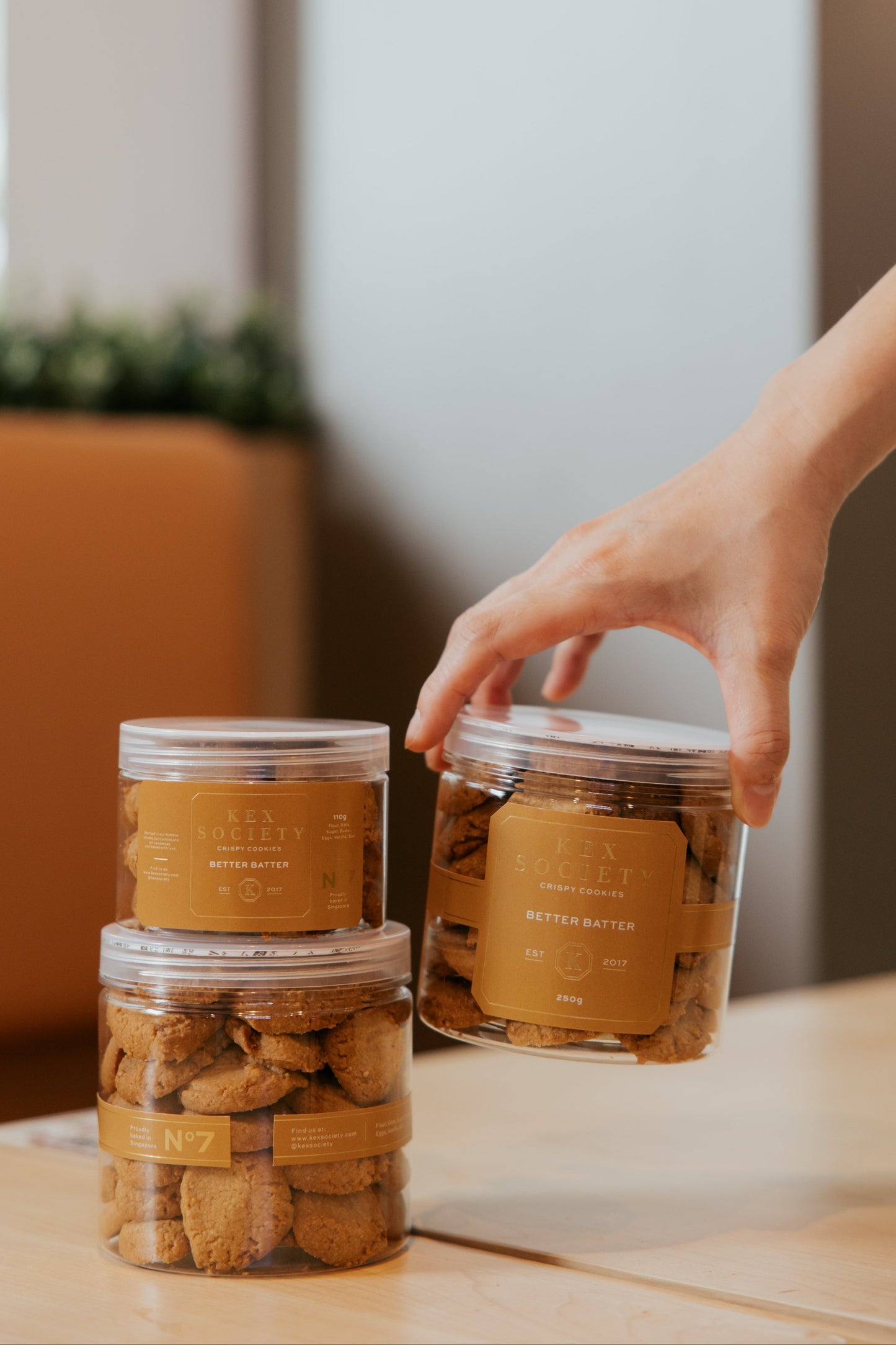 Person reaching for a jar of better batter cookies on a table with a blurred background