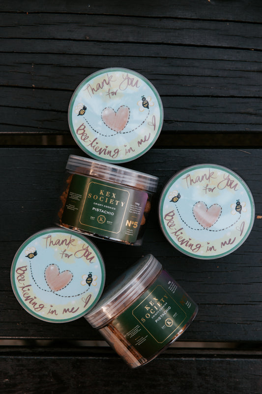Kex Society mini pistachio cookie bottles with teacher's day themed lids on a dark wooden surface